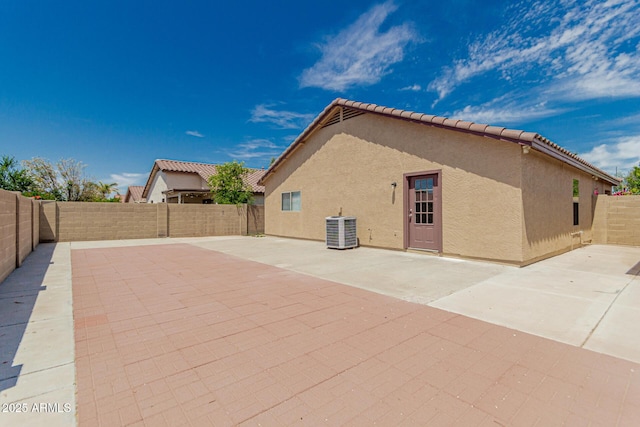 exterior space with a tile roof, central AC unit, a patio area, a fenced backyard, and stucco siding
