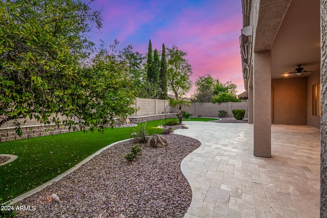 yard at dusk with ceiling fan and a patio area