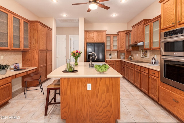 kitchen with a kitchen breakfast bar, a kitchen island with sink, tasteful backsplash, and black appliances