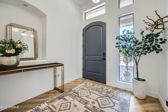 foyer featuring arched walkways, light wood-type flooring, and baseboards