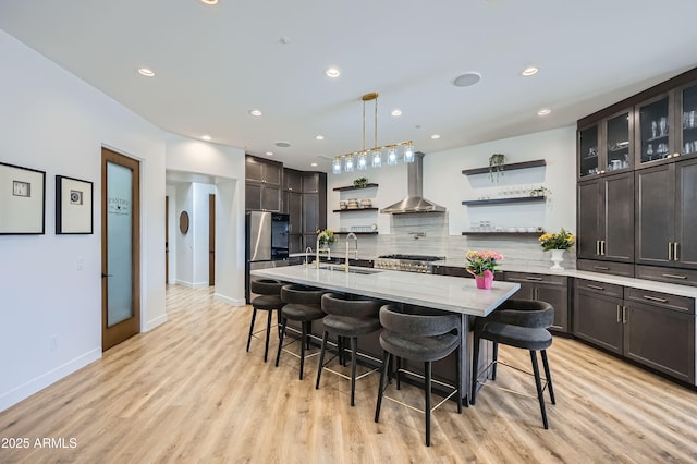 kitchen featuring open shelves, a sink, wall chimney exhaust hood, decorative backsplash, and light wood-style flooring