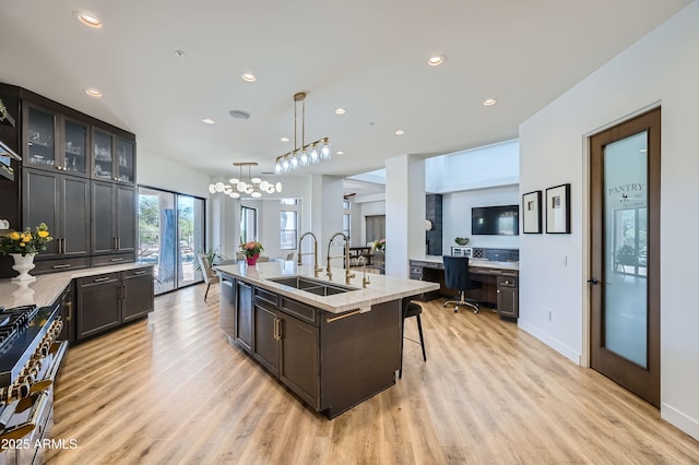 kitchen with a kitchen island with sink, a sink, light wood-style floors, and a breakfast bar area