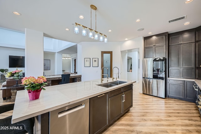 kitchen with a sink, visible vents, pendant lighting, light stone countertops, and appliances with stainless steel finishes