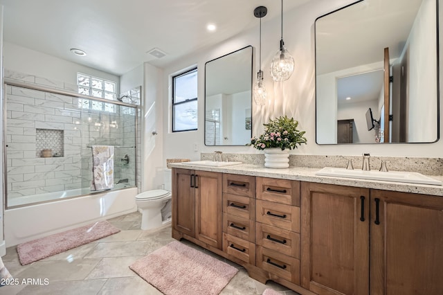 bathroom featuring a sink, bath / shower combo with glass door, double vanity, and toilet
