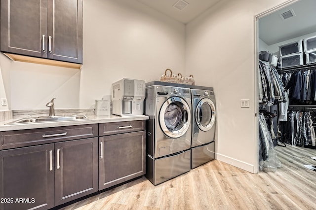clothes washing area with visible vents, light wood finished floors, a sink, and washer and clothes dryer