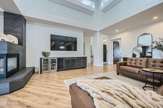 living room featuring light wood finished floors, a towering ceiling, baseboards, recessed lighting, and a tile fireplace