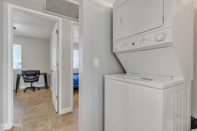 washroom with stacked washer / dryer, a healthy amount of sunlight, and light tile patterned floors