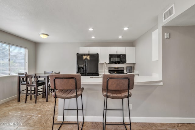 kitchen featuring a breakfast bar area, kitchen peninsula, sink, black appliances, and white cabinetry