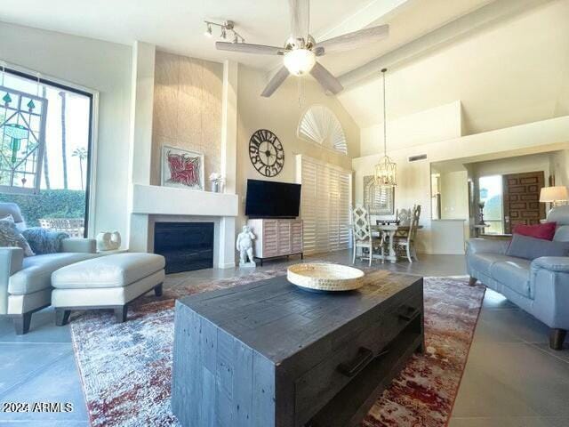 living room featuring beam ceiling, a wealth of natural light, a large fireplace, and ceiling fan with notable chandelier