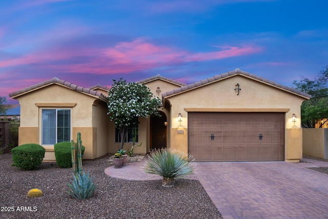 mediterranean / spanish house with stucco siding, a garage, decorative driveway, and a tile roof