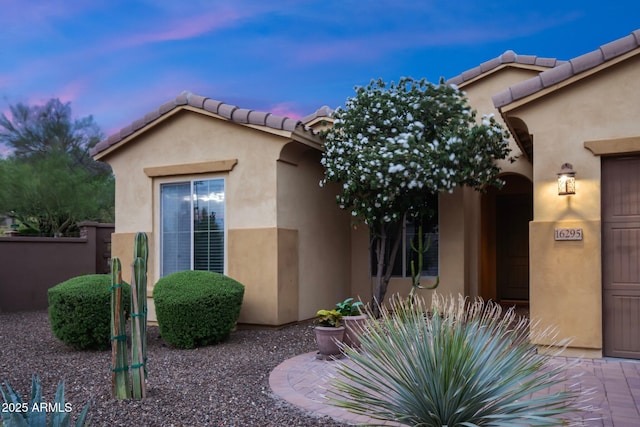 view of front of property featuring stucco siding, a tile roof, and fence