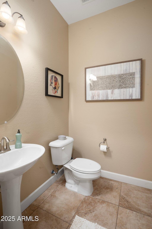 half bathroom with toilet, baseboards, and tile patterned floors