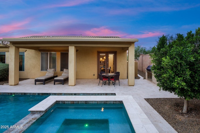 back of house at dusk featuring stucco siding, exterior kitchen, an outdoor pool, and a patio area