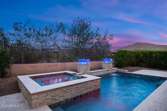 pool at dusk featuring exterior kitchen, a fenced backyard, and an in-ground hot tub