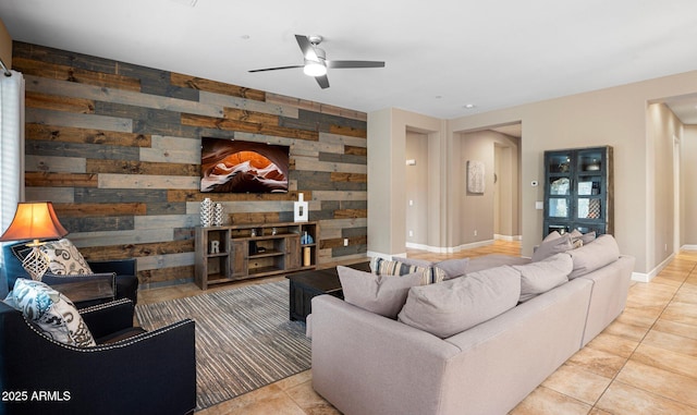 living area with wooden walls, ceiling fan, tile patterned flooring, and baseboards