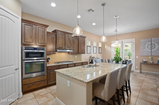 kitchen with a sink, stainless steel appliances, light tile patterned floors, under cabinet range hood, and tasteful backsplash