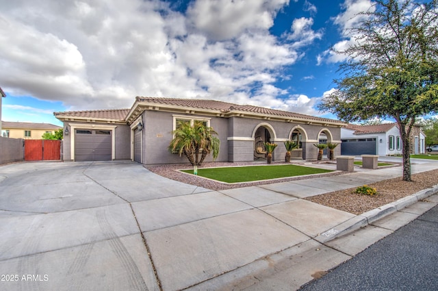 mediterranean / spanish-style house featuring stucco siding, a tile roof, fence, concrete driveway, and an attached garage