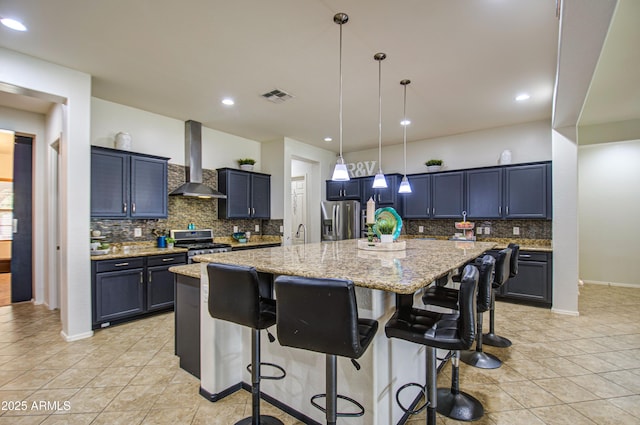 kitchen featuring visible vents, a kitchen bar, appliances with stainless steel finishes, wall chimney exhaust hood, and light stone countertops