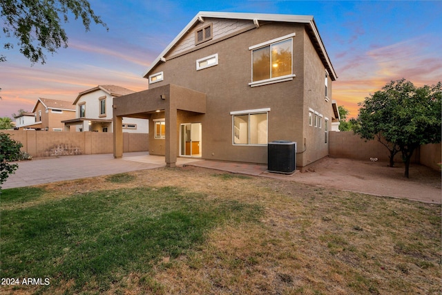 back house at dusk with a yard, cooling unit, and a patio