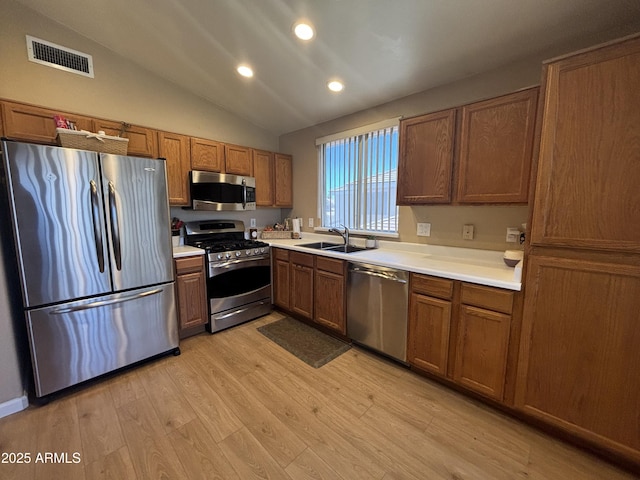 kitchen with appliances with stainless steel finishes, a sink, brown cabinetry, light wood-style flooring, and lofted ceiling