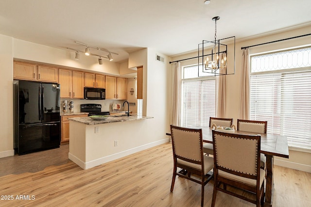 kitchen with light wood-type flooring, kitchen peninsula, pendant lighting, light stone countertops, and black appliances