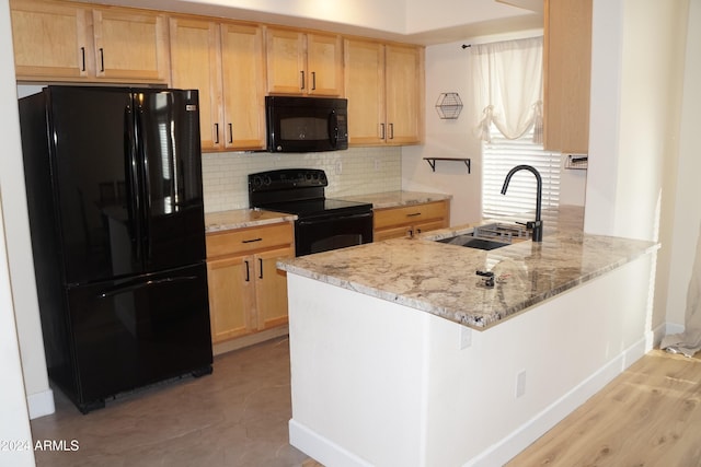 kitchen with kitchen peninsula, sink, light stone countertops, and black appliances