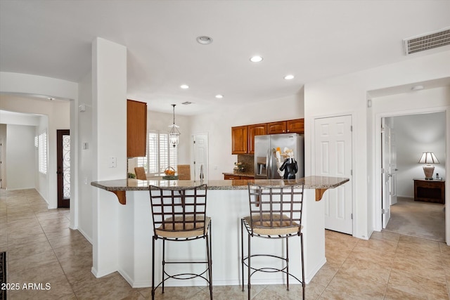 kitchen with stainless steel refrigerator with ice dispenser, a kitchen bar, dark stone countertops, kitchen peninsula, and pendant lighting