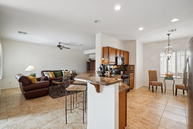 kitchen featuring a kitchen bar, decorative light fixtures, kitchen peninsula, dark stone counters, and black appliances