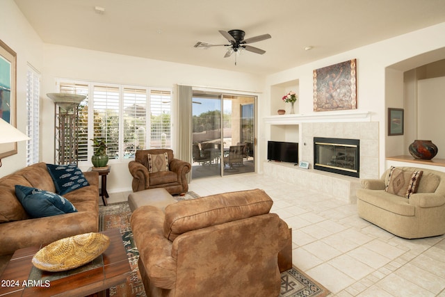 tiled living room with ceiling fan, a tile fireplace, and built in shelves