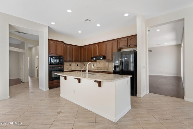 kitchen featuring a breakfast bar, a center island with sink, black appliances, backsplash, and light tile patterned floors