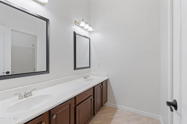 bathroom with baseboards, double vanity, a sink, and tile patterned floors