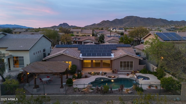 back of house at dusk featuring a tile roof, stucco siding, a patio, a fenced backyard, and solar panels