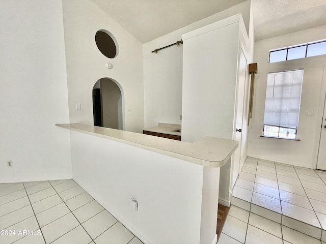 kitchen with white cabinets, kitchen peninsula, a high ceiling, and light tile patterned floors