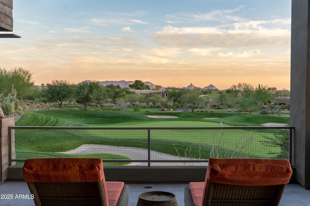 balcony at dusk featuring golf course view and a mountain view