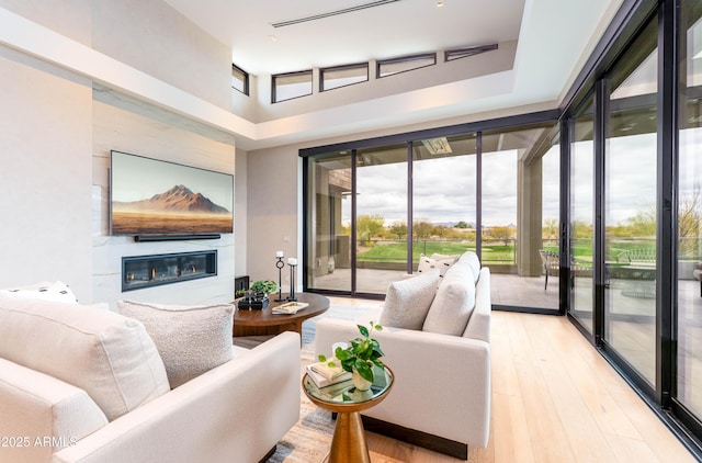 living room featuring a glass covered fireplace, light wood-style floors, and expansive windows