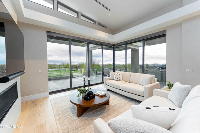 living room featuring light wood-style flooring, a fireplace, baseboards, and lofted ceiling