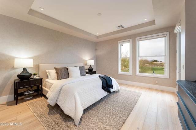 bedroom with visible vents, light wood-style flooring, baseboards, and a tray ceiling