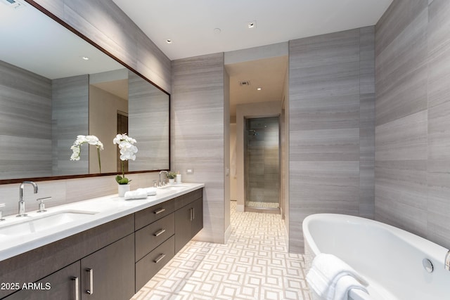 bathroom featuring a freestanding bath, tile walls, tiled shower, and a sink