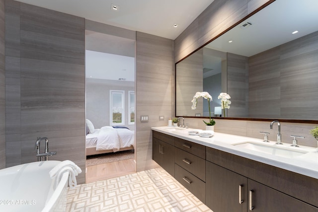 ensuite bathroom featuring tile walls, a soaking tub, and a sink