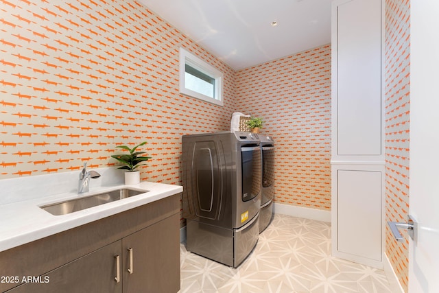 laundry area featuring washing machine and clothes dryer, wallpapered walls, baseboards, cabinet space, and a sink