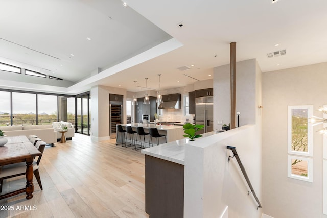 kitchen featuring visible vents, open floor plan, a breakfast bar area, range hood, and built in fridge