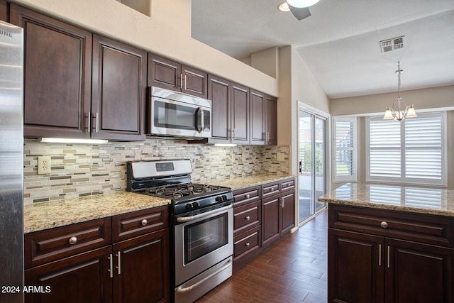 kitchen featuring lofted ceiling, light stone counters, hanging light fixtures, stainless steel appliances, and decorative backsplash