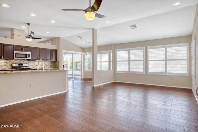 kitchen with appliances with stainless steel finishes, lofted ceiling, backsplash, light stone counters, and dark brown cabinets