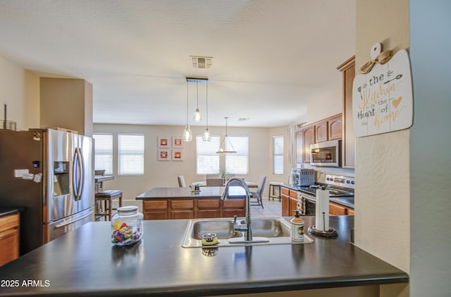 kitchen featuring a center island, brown cabinets, a sink, dark countertops, and stainless steel appliances