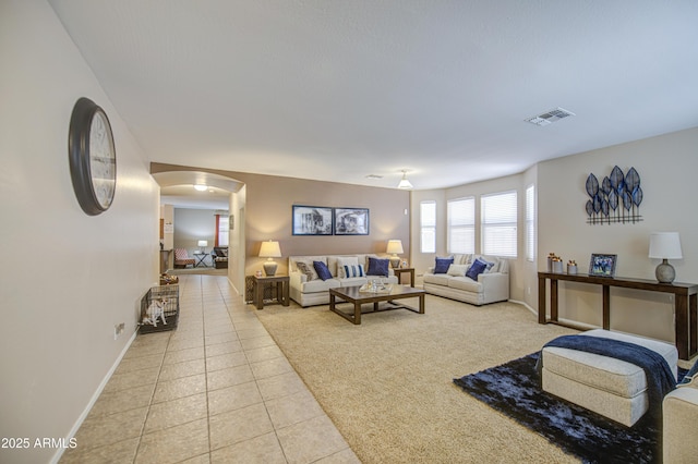 living area featuring visible vents, baseboards, light tile patterned flooring, and arched walkways