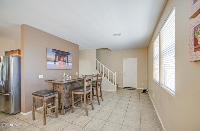 dining room featuring light tile patterned floors, baseboards, visible vents, wet bar, and stairs
