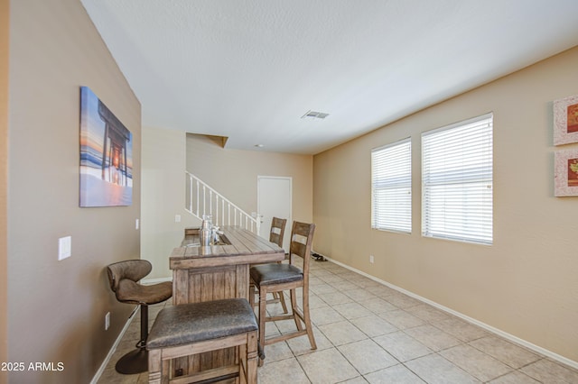 dining space with light tile patterned floors, visible vents, baseboards, and stairway