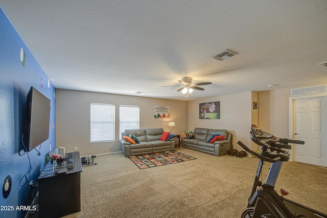 carpeted living area featuring a textured ceiling, visible vents, baseboards, and a ceiling fan