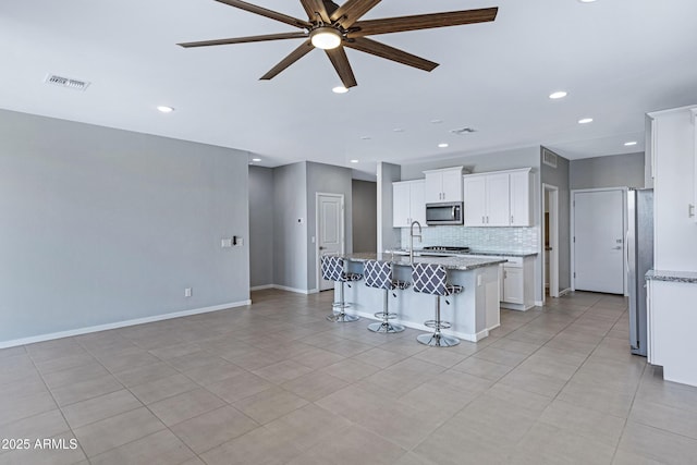 4628 W Greenleaf Dr, San Tan Valley, AZ 85144 - kitchen featuring appliances with stainless steel finishes, ceiling fan, decorative backsplash, a kitchen breakfast bar, and white cabinetry