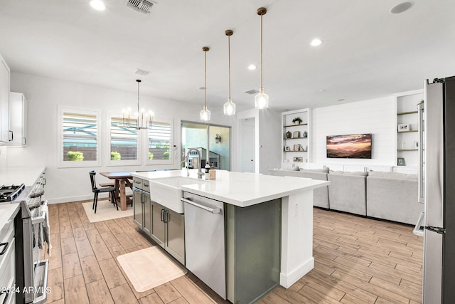 kitchen featuring light wood-type flooring, an island with sink, white cabinetry, stainless steel appliances, and decorative light fixtures